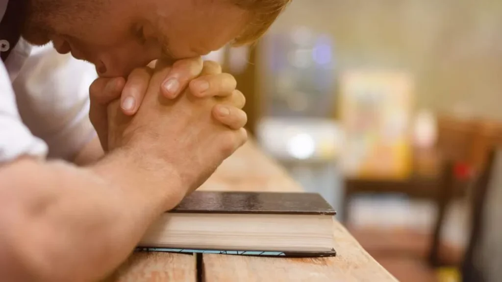 Imagem homem orando apoiado na biblia do artigo Pode o católico frequentar uma igreja evangélica?