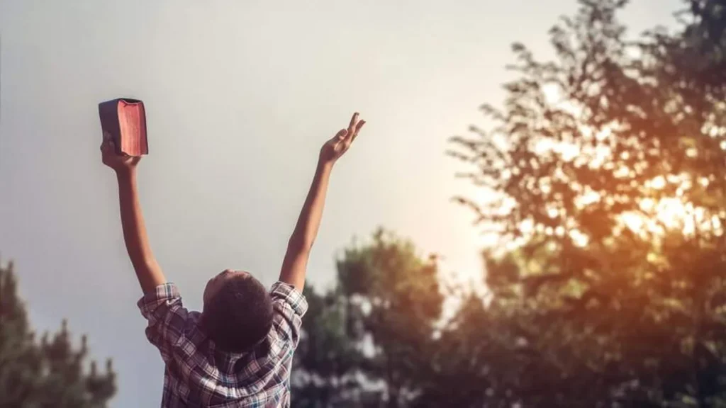 Imagem jovem bracos erguidos com biblia do artigo Homilia JM: Transforme sua vida em um louvor agradável a Deus!