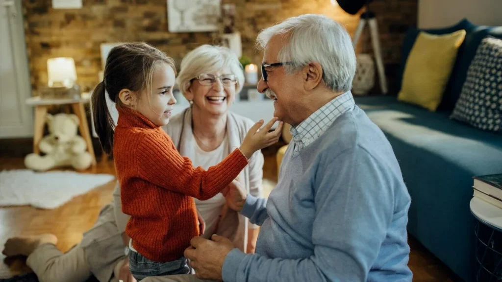Imagem Uma menina sorrindo com seus avos fazendo carinho no rosto de seu avo do artigo Por que devemos valorizar o relacionamento com nossos avós?