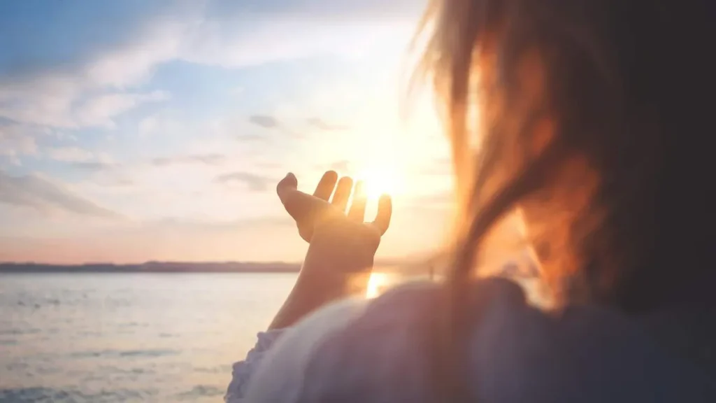 Imagem Mulher de costas com mao iluminada pelo sol na beira do mar do artigo Olhe o futuro com esperança