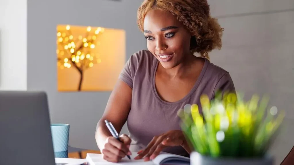 Imagem mulher se planejando pelo caderno olhando o notebook do artigo Concretize seus sonhos em 2023 com essas 2 dicas!