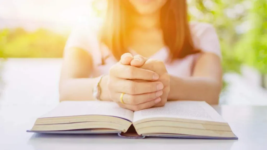 Imagem Mulher com as maos em posicao de oracao e sobre a Biblia do artigo Como posso meditar na Palavra de Deus?