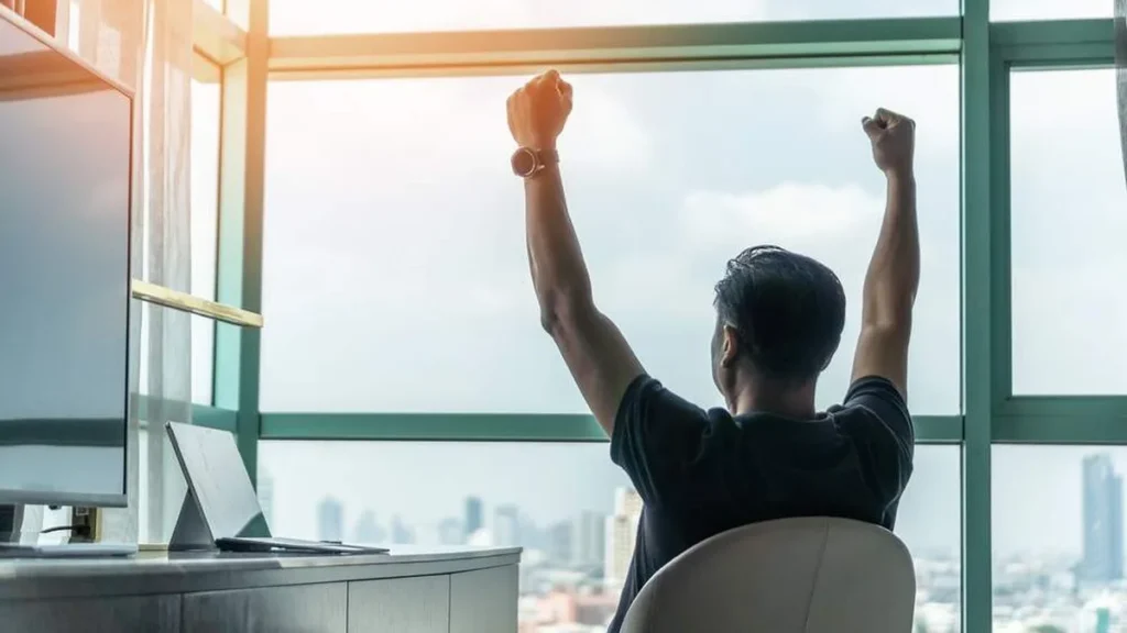 Imagem homem comemorando sentado no trabalho do artigo Obtenha alta performance no trabalho e na vida!