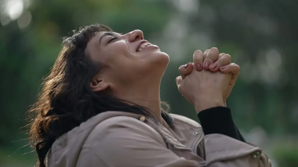 Imagem Mulher sorrindo olhando para cima como maos em posicao de oracao do artigo Dia Mundial da Oração: o fio que conecta o homem a Deus