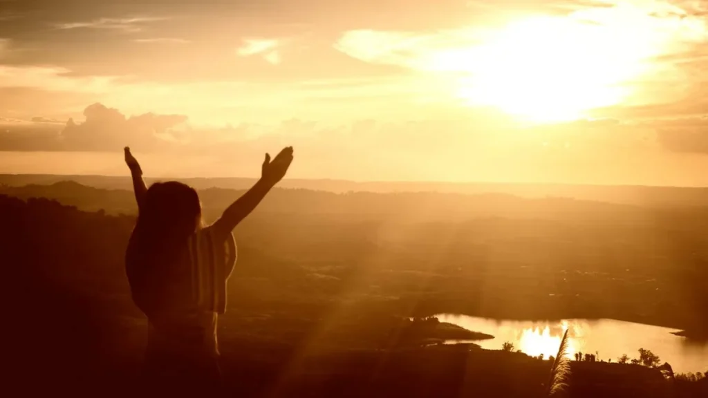 Imagem menina com bracos abertos enquanto o sol lhe ilumina do artigo 5 conselhos de Santos para uma vida mais próxima de Deus