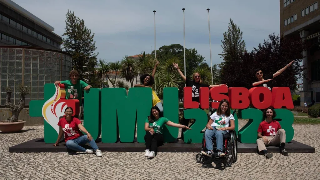 Imagem Jovens sorrindo a frente do letreiro da JMJ de Lisboa do artigo JMJ: Rise up deste mês reflete o “Grande Anúncio do Amor de Deus”