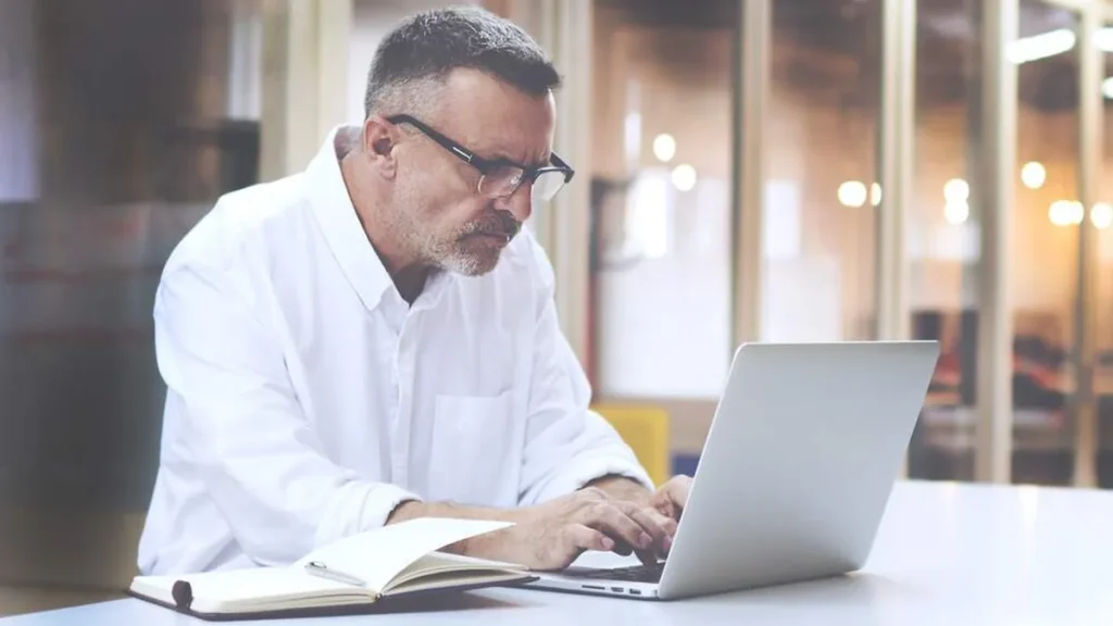 Imagem homem grisalho trabalhando com notebook do artigo Quero mudar de profissão, mas me sinto velho. E agora?