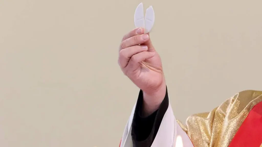 Imagem Maos de padre segurando hostia partida fracao do pao eucaristia do artigo Por que o padre quebra um pedaço da hóstia e coloca dentro do cálice?
