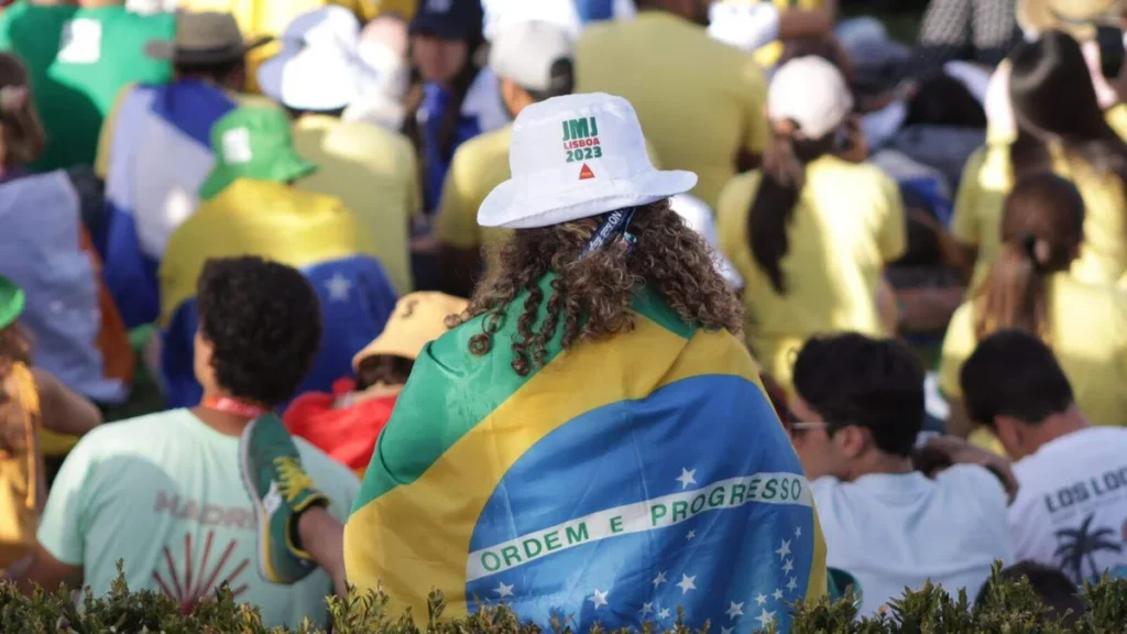 Jovem de costas com bandeira do Brasil e chapéu da JMJ Lisboa