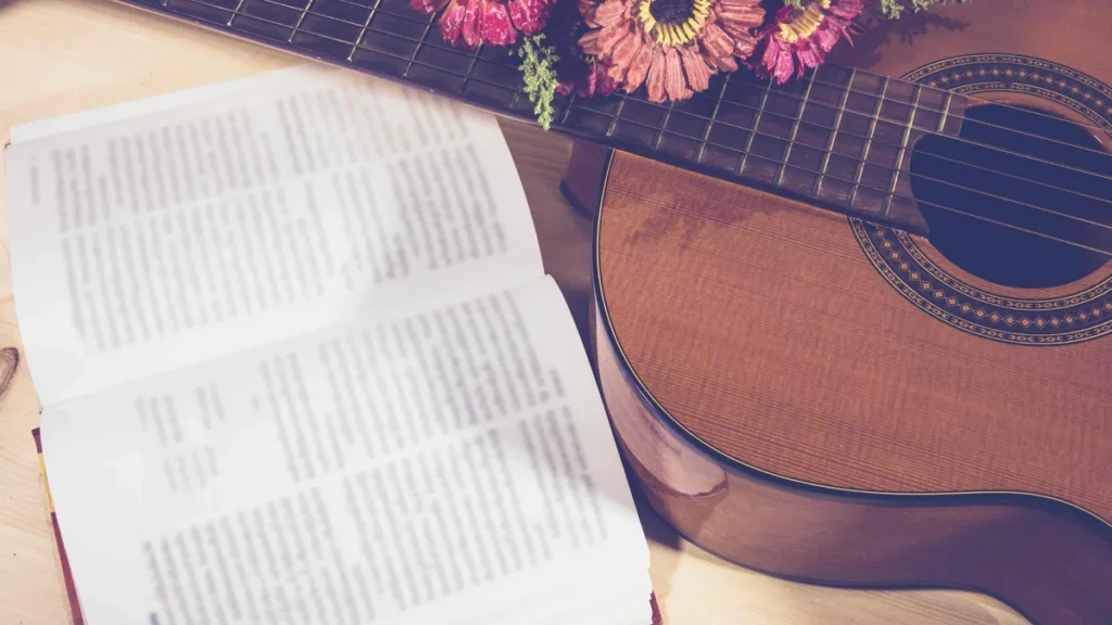 Imagem violao sob a mesa ao lado de flores e uma Biblia do artigo Dia do compositor: Santos e personagens bíblicos com o dom para música