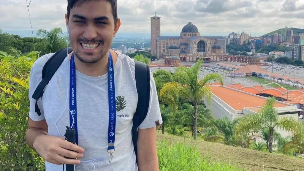 Descrição da imagem: Gustavo está na frente do Santuário Nacional de Aparecida, com uma vista panorâmica para o centro de peregrinação