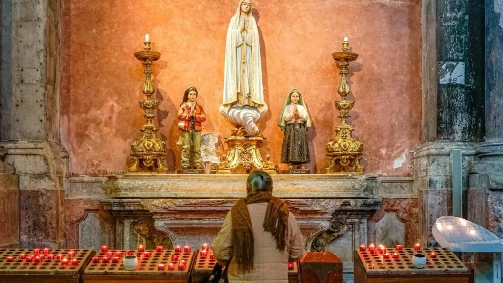 Imagem mulher rezando dentro de igreja em frente a um oratorio com a imagem de nossa senhora de fatima e os pastorinhos do artigo Filme do Dia: Fátima, A História de um Milagre