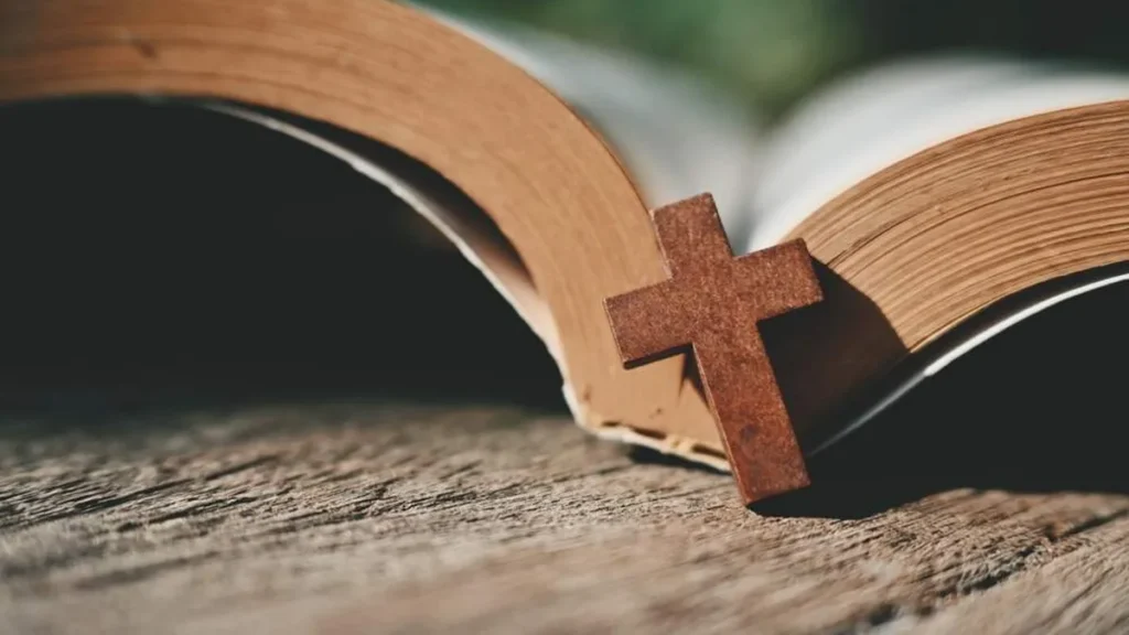 Imagem biblia aberta sobre uma mesa com uma cruz de madeira sobreposta do artigo O que Carlo Acutis e José de Anchieta têm em comum?