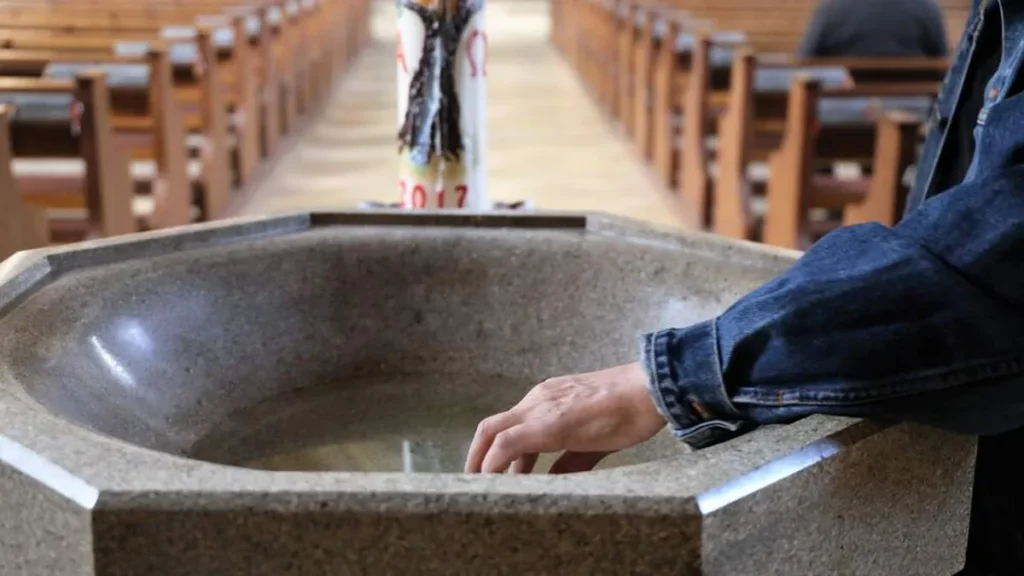 Imagem pessoa molhando a mao com agua benta dentro da igreja do artigo Como usar água benta no dia a dia?