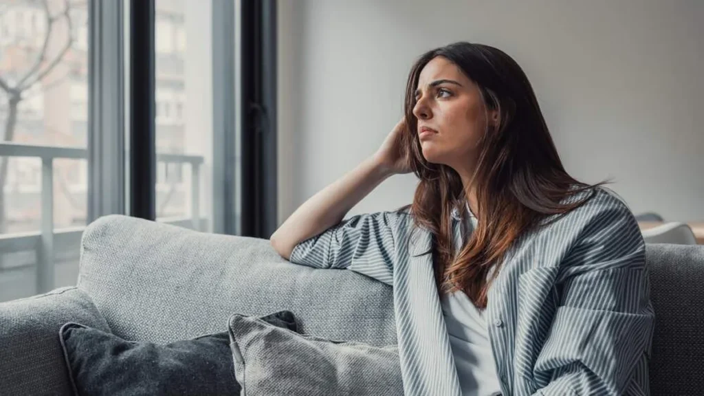 Imagem mulher sentada no sofa e pensativa do artigo Como a fé pode ser um auxílio contra a ansiedade?