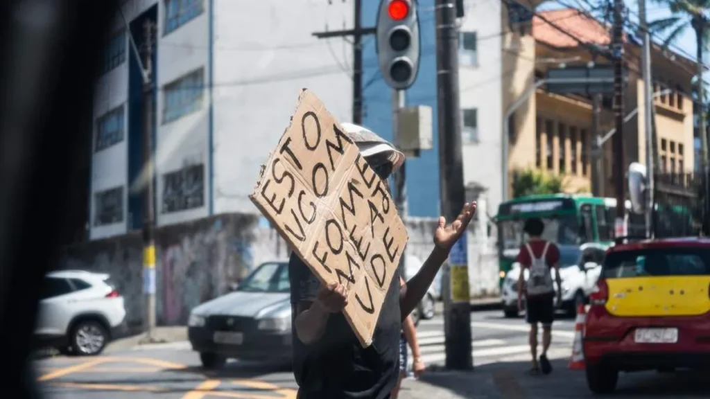 Imagem pessoa pede ajuda com cartaz em semaforo fome pobreza do artigo Cuidar daqueles que sofrem: a urgência da caridade no mundo de hoje