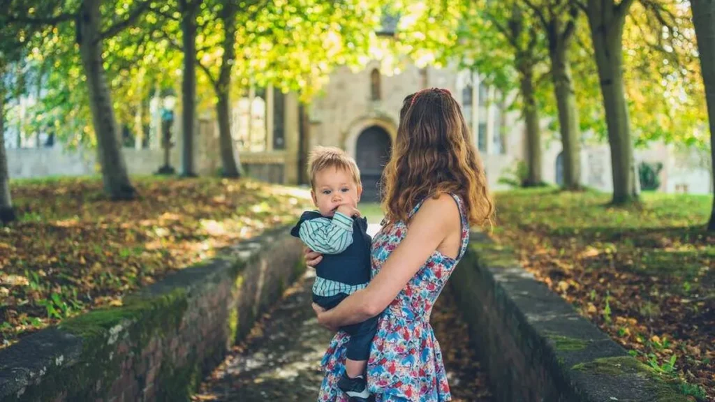 Imagem mulher segurando bebe na frente da igreja do artigo O que é a apresentação de crianças na Igreja?
