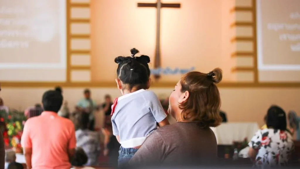 Imagem mae com filha na igreja durante missa do artigo Como incentivar meus filhos a serem ativos na Igreja?