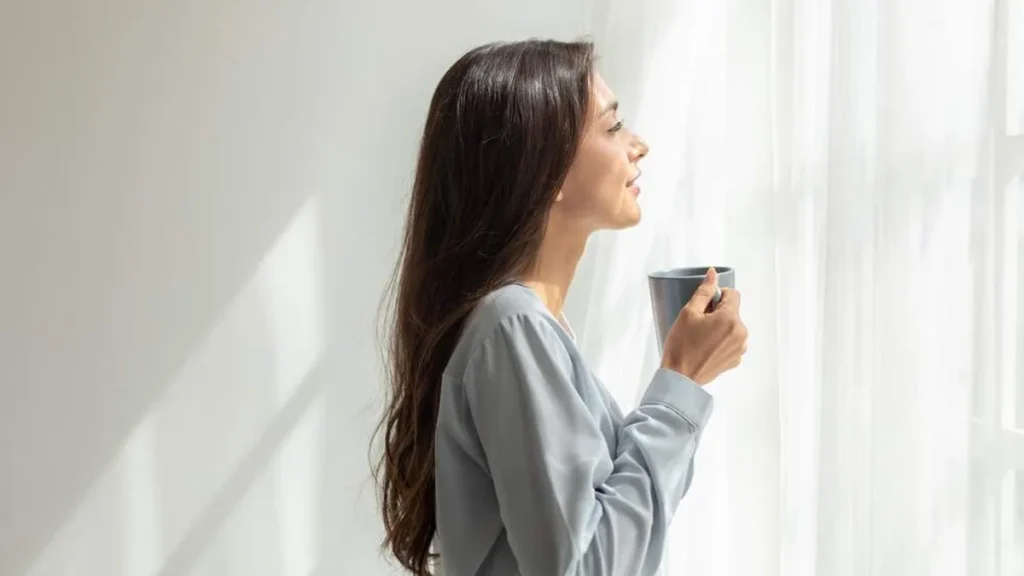 Imagem Mulher com uma xicara nas maos olhando pela janela do artigo Como confiar plenamente nos planos de Deus?