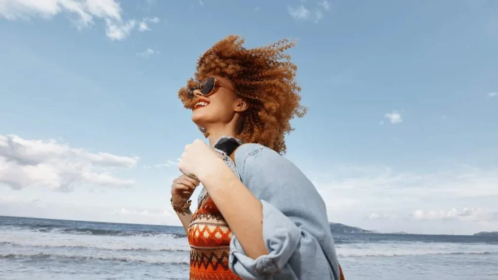 Imagem mulher feliz andando pela praia do artigo Vale tudo para ser feliz?