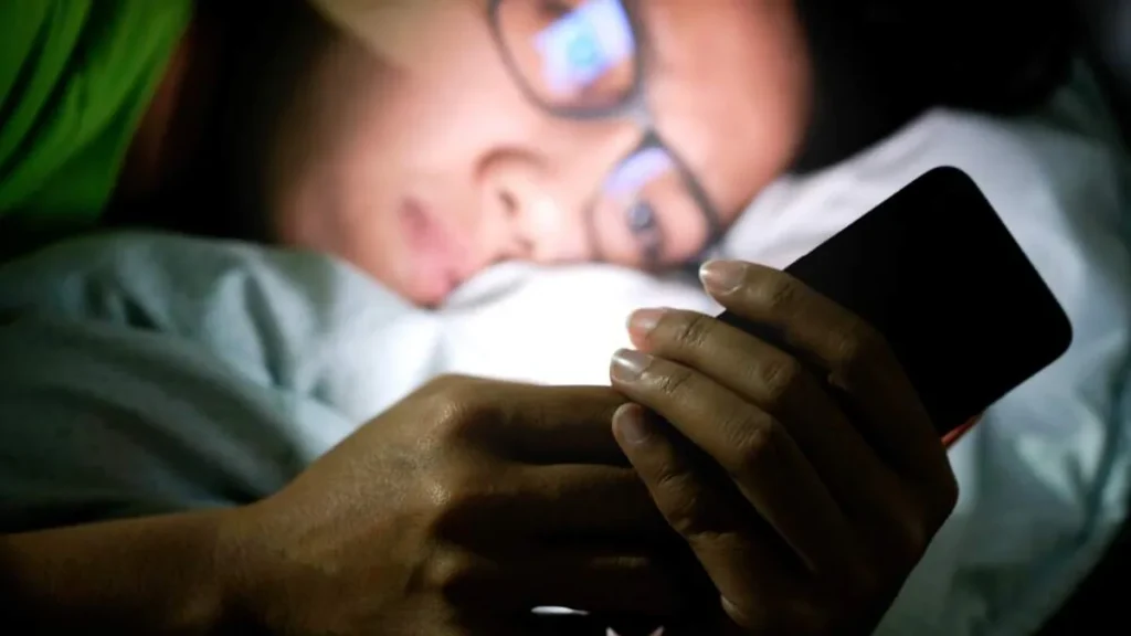 Imagem pessoa deitada na cama olhando o celular do artigo Papa para intenção de abril: "olhar nos olhos, menos para as telas"