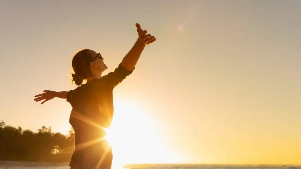 Imagem Mulher na praia com os bracos abertos e por do sol do artigo Esperança e Sonhos: o caminho para uma vida com sentido