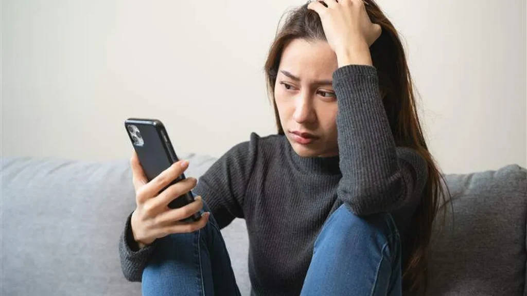 Imagem Mulher segurando o celular com a mao na cabeca com a expressao triste do artigo O silêncio por trás das notificações