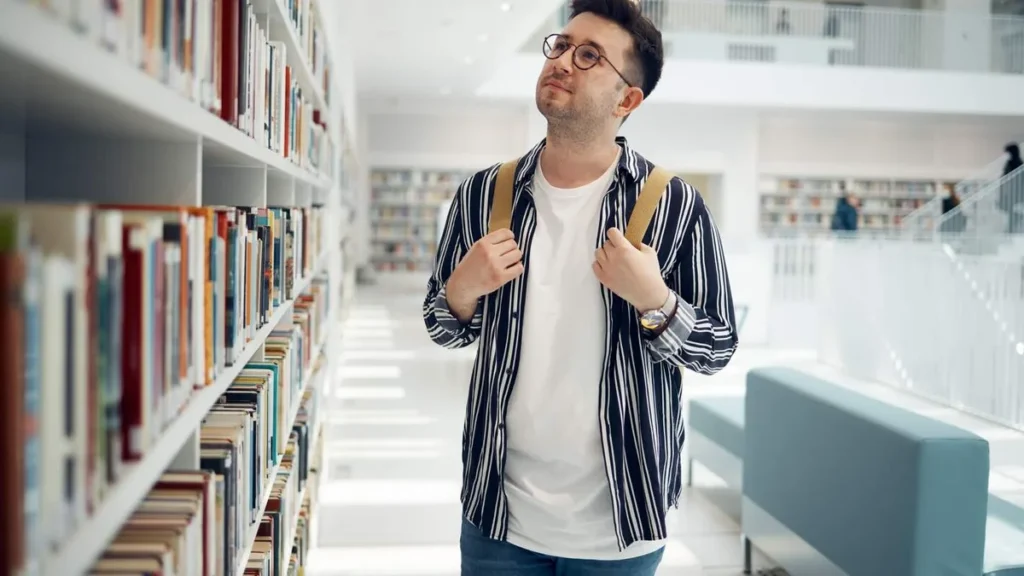 Imagem moco de mochila em uma biblioteca escolhendo qual livro ler do artigo Filosofia para a vida: 6 livros que vão abrir sua mente!