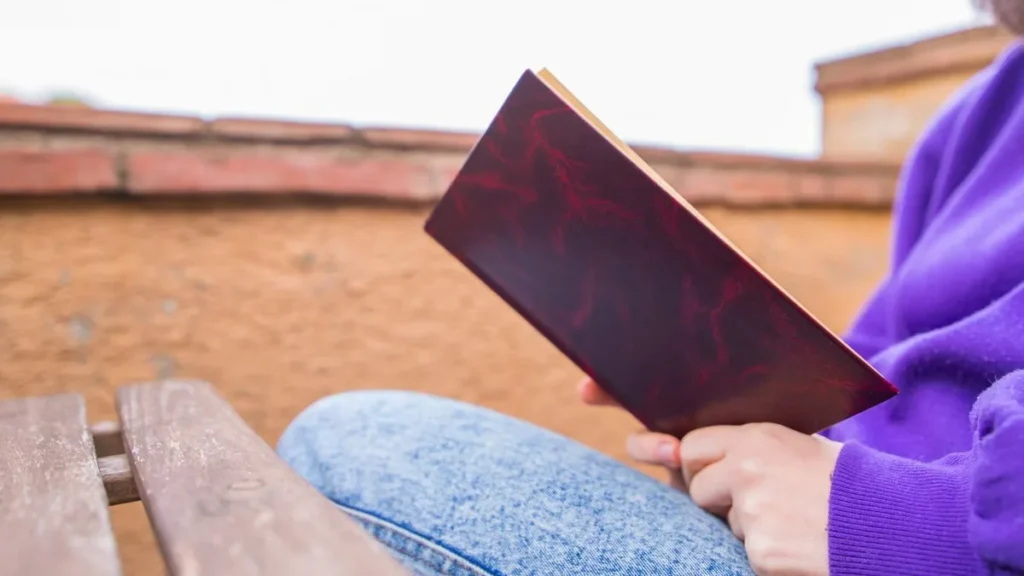 Imagem pessoa lendo um livro com foco nas maos e na capa do livro do artigo Entre riscos e rabiscos: livro propõe poesia que cura o silêncio