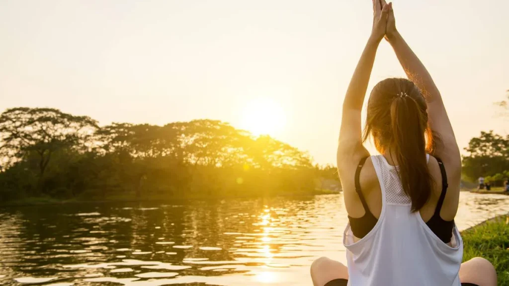 Imagem Mulher meditando diante do por do sol do artigo A arte de bem viver: três princípios para uma vida feliz