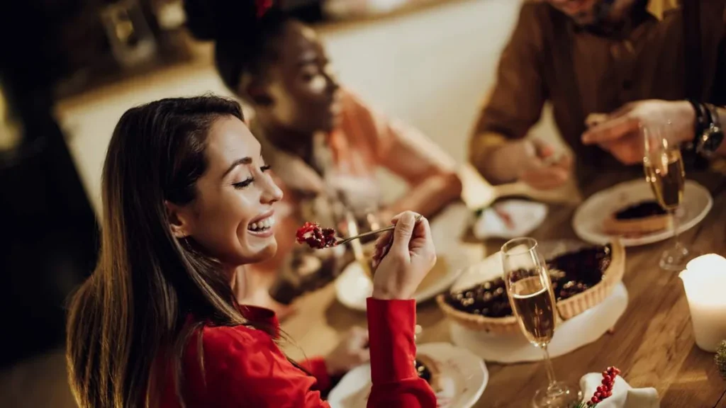 Imagem mulher feliz comendo torta alegre enquanto jantando de natal com amigos em casa Easy Resize.com do artigo Festas de fim de ano e alimentação, é possível equilibrar?