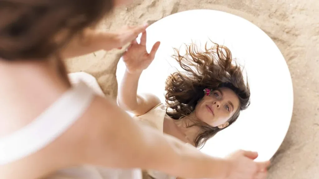 Imagem Mulher se olhando no espelho em um gesto de amor proprio do artigo A força do amor-próprio na construção do bem-estar