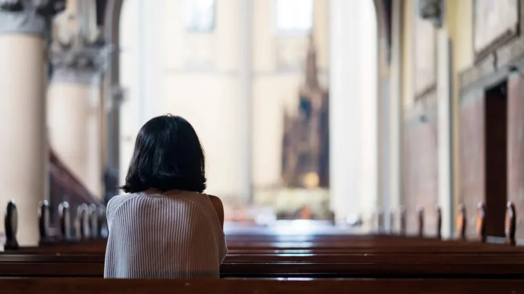 Imagem mulher rezando ajoelhada na igreja do artigo Quando e como a Igreja orienta fazer a Comunhão Espiritual?
