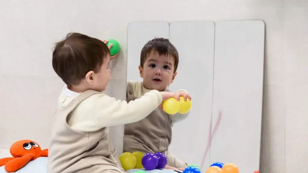 Imagem bebe brincando com bolinhas de frente pro espelho do artigo Livro explica que bebê ‘vira gente” após nascimento psíquico
