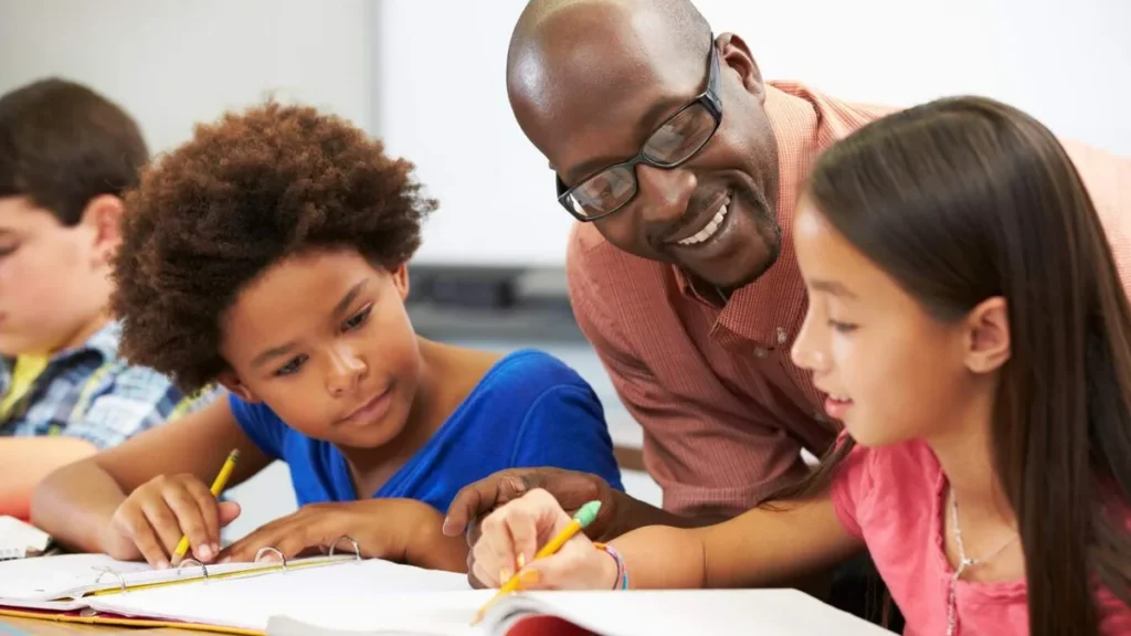Imagem professor sorrindo com alunos criancas ensinando licao do artigo Piso salarial dos professores passa a ser de R$ 5.130